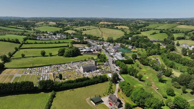Patrick Kavanagh Centre, Inniskeen Village, County Monaghan, Ireland, June 2023. Drone orbits clockwise high above St. Mary's Church with rolling lush green hills on a bright summer day.