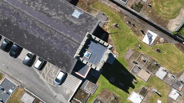 Patrick Kavanagh Centre, Inniskeen Village, County Monaghan, Ireland, June 2023. Drone in Bird's Eye view tracks over the cemetery plots to St. Mary's Church spire and rises in a rotating ascent.