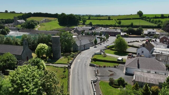 Inniskeen Village, County Monaghan, Ireland, June 2023. Drone pushes forward over the river Fane along a road to establish roundabout as cars drive by on a warm summer day.