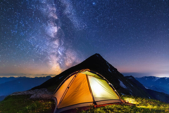Tent illuminated from the inside with the Milky Way in the background.