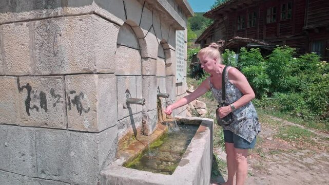Woman cools off using village free refreshing spring water on hot day