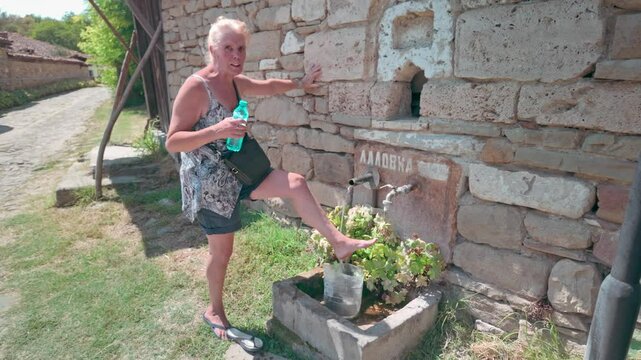 Woman cools bare feet on hot day using village spring water