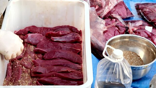 Venison steak strips stacked in white plastic container to be preserved with vinegar and mixed herbs with salt to make South African delicacy of biltong
