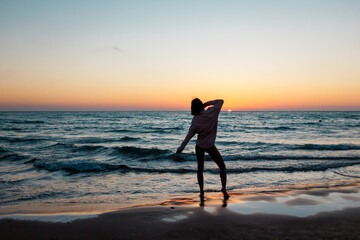 Silhouette of a woman watching the sunset on the beach. Summer mood.