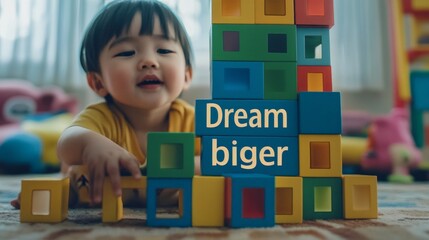 A toddler playing with building blocks, text "Dream big, build bigger" on the block tower