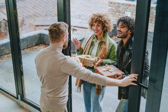 Man welcoming guests on holiday with gifts near door at home - Powered by Adobe