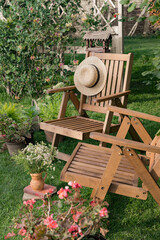 Garden wooden furniture on the lawn. Two wooden armchairs, next to vases with flowering plants. A pergola with wicker plants in the background. Beautiful landscape with garden furniture. 