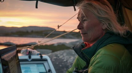 Obraz premium Elderly Woman Working on Laptop in Tent During Sunset Camping in Nature, Emphasizing Outdoor Adventure, Technology Use, and Active Senior Lifestyle