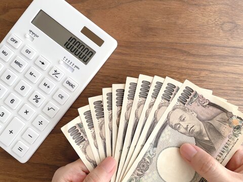 机の上で10万円を持つ女性の手と電卓