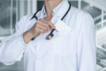 A doctor in a white coat takes a business card out of his pocket.