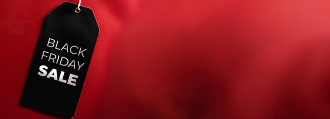 Black tag with white BLACK FRIDAY SALE text on red dark background, free copy space, long wide poster template background discount retail promotion and holiday sales.