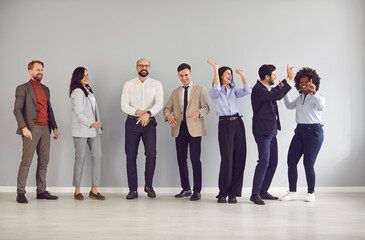 Obraz premium Happy multinational business people team in business casual clothes dancing and celebrating success after successful project. Cheerful diverse colleagues having a party against a gray wall backdrop.