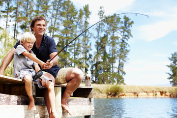Father, boy and fishing by lake for development, vacation and travel together in summer with gear on dock. Dad, son and catch fish in nature for learning, holiday and teaching while bonding with help