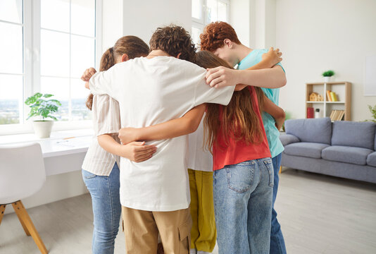 Group of teenage students embracing each other in a circle at cozy home. The diverse team of friends stands together, symbolizing unity and strong connection in a home environment.