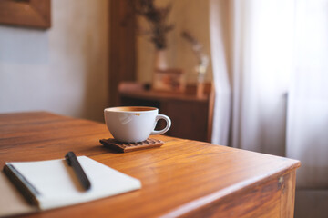A coffee cup with notebook and a pen on wooden table