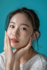 Fototapeta premium Beautiful Asian Woman with Long Hair Posing with Hands on Chin Against Turquoise Background