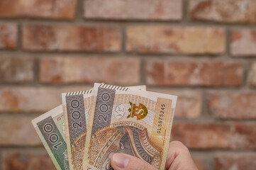 Polskie pieniądze w dłoni. Gotówka na tle murowanej cegły,  koszt materiałów budowlanych