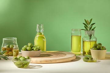 On a green background, fresh olives, leaves and oil of olive containing in many glass flasks. Front view and empty space for design. Minimal concept for advertising product with olive extract