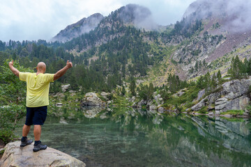 Naklejka premium Rear view of a hiker in a rock with raised arms, looking the landscape.