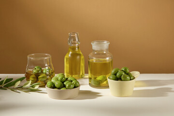 Fresh green olives on bowls and olive oil on glass bottle decorated on brown background. Front view, advertising scene for product cosmetic with natural extract, natural ingredient