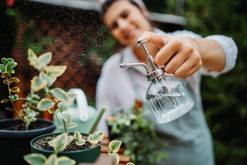 Young woman taking care of plants with water can and mister in garden
