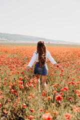 Woman poppies field. Back view of a happy woman with long hair in a poppy field and enjoying the beauty of nature in a warm summer day.