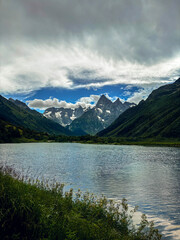 An alpine lake in Caucasus region on a summer day. The sky is dramatic bright blue with storm clouds. The mountains are velvet green. 