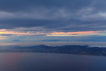 Sunset over a city at seaside near mountains. Aerial view of the ocean and mountains, showcasing the stunning landscape from an airplane window