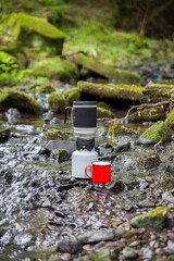 Coffee pot and metal cup on a large stone against the background of a mountain river. Coffee pot on a stone slab against a blurred background of nature.