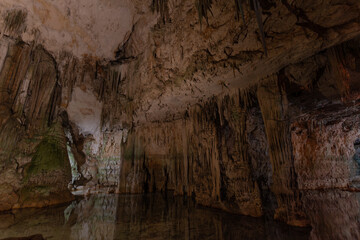 Large cavern flooded with water in the Grotto of Neptune in Sardinia, Italy, with large columns and stalactites reflected in the water, with no people. Tourist concept in Sardinia island