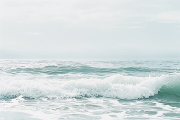 Fototapeta premium Gentle ocean waves crash and roll under a soft, overcast sky, capturing the serene and calming essence of the sea.