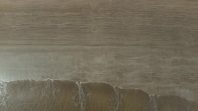 Barrido de olas blancas que crean un efecto de s&aacute;banas en la arena que es captado por un drone en 4k. Este espect&aacute;culo natural se crea desde las alturas y toca la arena amarilla, azul y atardeceres.