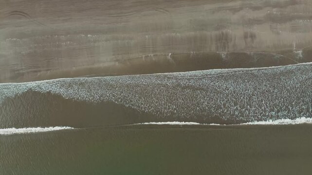 Barrido de olas blancas que crean un efecto de s&aacute;banas en la arena que es captado por un drone en 4k. Este espect&aacute;culo natural se crea desde las alturas y toca la arena amarilla, azul y atardeceres.