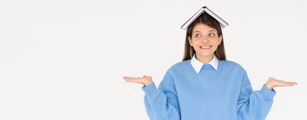 Portrait of funny young smiling student girl with an open book on her head with raised hands having...