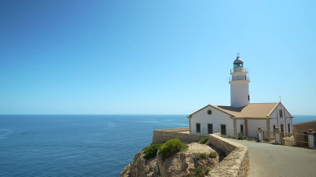 Capdepera Lighthouse perched on a rugged cliff, overlooking the vast and calm Mediterranean Sea in Mallorca. The clear blue sky and tranquil waters create a serene and captivating scene, highlighting
