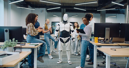 Robot staying in middle of room. Group of multi-ethnic coworkers clapping. Multi-ethnic group of...