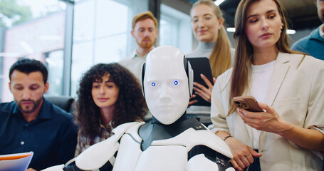 Multi-ethnic group of people surrounding robot. Giving command to press specific key on keyboard in...