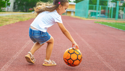 childhood, leisure games and people concept - happy little girl with ball playing soccer at school field