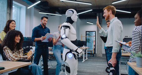 Multi-ethnic group of people gathering together to watch humanoid robot perform simple tasks. Asking questions and discussing results. Noting everything down on notepad. Man communicating with cyborg.