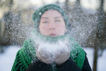 Teen girl blows fresh snow in cold winter day