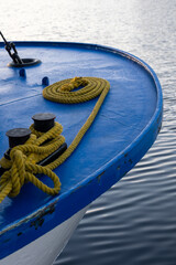 Fototapeta premium Close-up of a blue boat's edge with coiled rope and cleats on a calm water surface during sunset