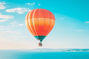 Fototapeta premium A striking image showing a colorful hot air balloon with vibrant orange and red hues, floating above an expansive blue sea and distant coastline under a sunny sky.
