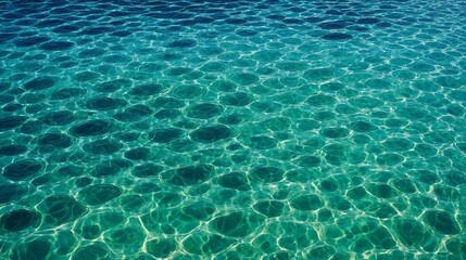 Obraz premium Close-up of clear ocean water with unique circular patterns created by sunlight reflections. The turquoise and emerald hues blend beautifully, showcasing the tranquil and pristine water surface.