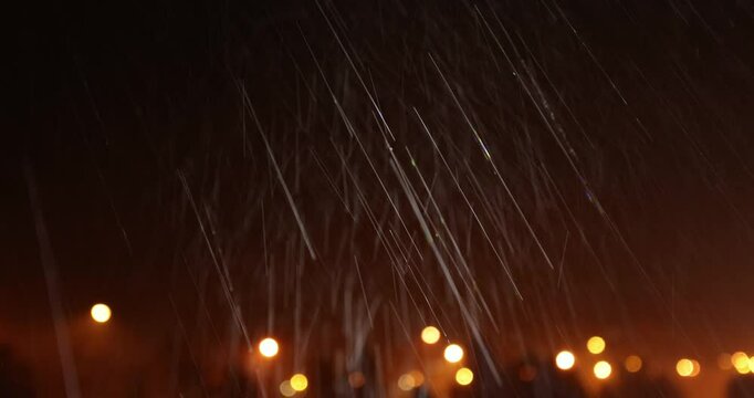 Real natural rain falling on camera against a blurred cityscape at night. Real time with sound.
