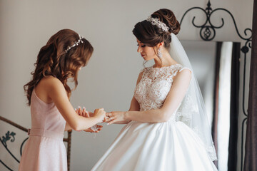 A bride and her bridesmaid are getting ready for the wedding. The bride is wearing a white dress...