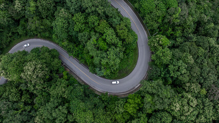 Aerial view car drive in green tree forest road winding road through the forest, Car drive on asphalt road between green tree forest, Electric vehicle EV car drive on asphalt road green tree forest.