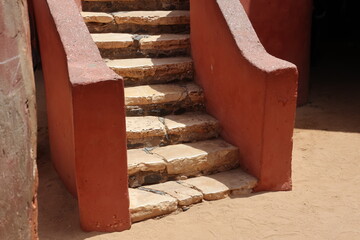 Vue d'un détail de l'escalier de couleur orangée de la maison des esclaves de l'île de Gorée au Sénégal. Rampe de forme incurvée. Architecture coloniale. Bâtiment rénové et coloré. Avril 2024.