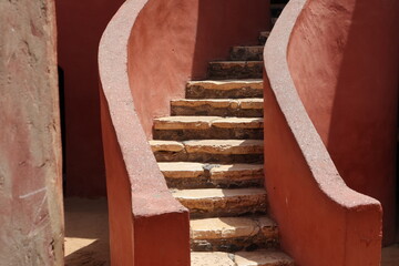 Vue d'un détail de l'escalier de couleur orangée de la maison des esclaves de l'île de Gorée au Sénégal. Rampe de forme incurvée. Architecture coloniale. Bâtiment rénové et coloré. Avril 2024.