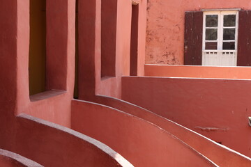 Vue d'un détail de l'escalier de couleur orangée de la maison des esclaves de l'île de Gorée au Sénégal. Rampe de forme incurvée. Architecture coloniale. Bâtiment rénové et coloré. Avril 2024.