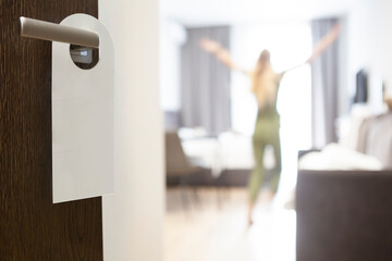 Privacy sign hanging on handle of open door to hotel room with standing person. Copy space.